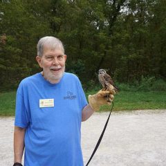 Man holding Kestrel in hand with trail and woods in background