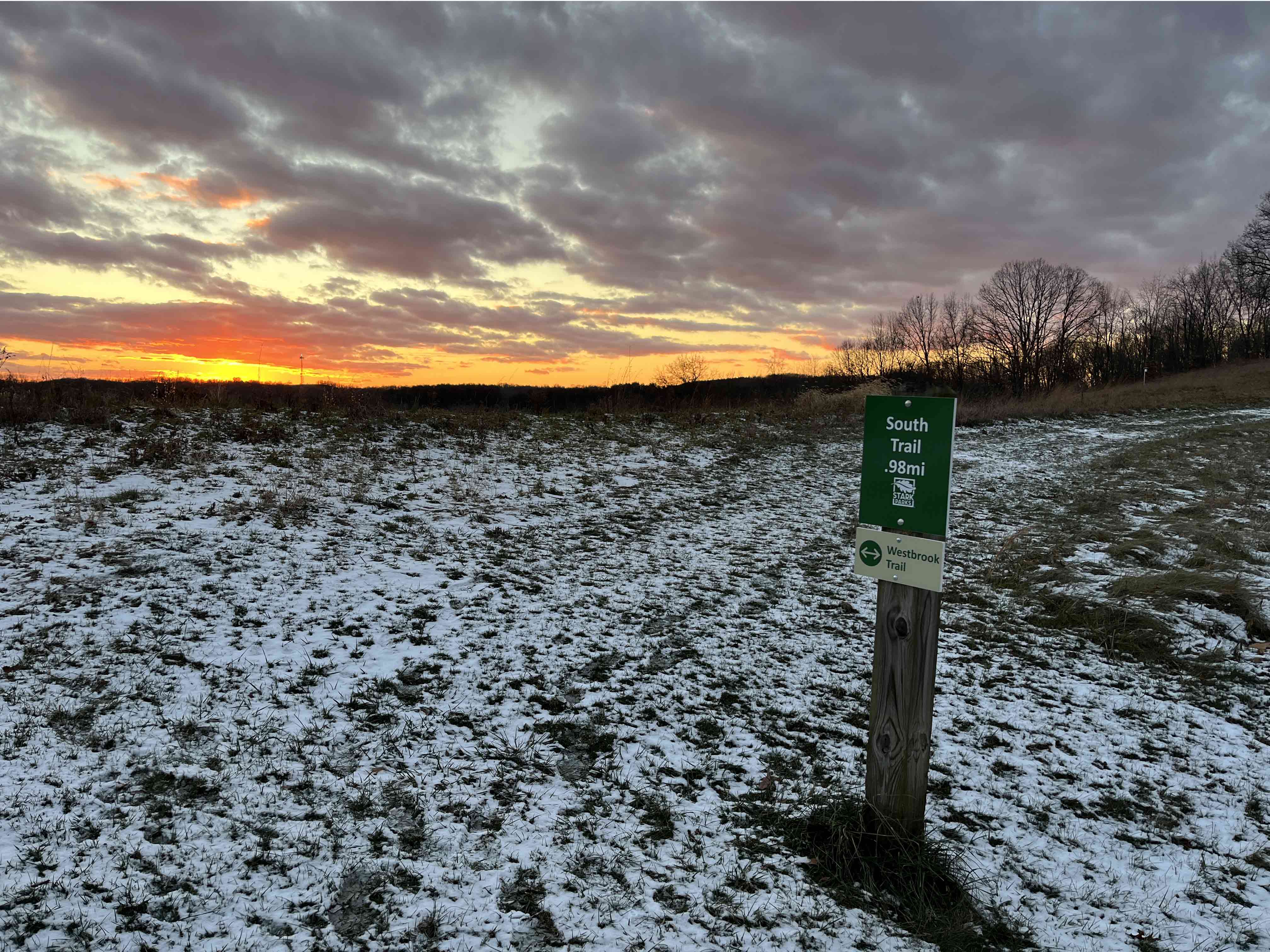 grass and snow popping up on trail with sign and post