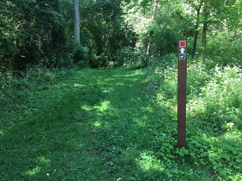 Sign with horseback riding stick on it next to trail
