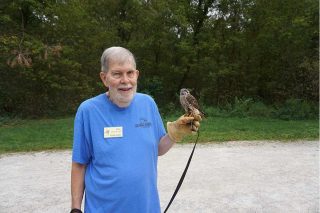 Man holding Kestrel in hand with trail and woods in background