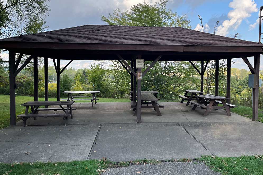 shelter with six picnic tables and trees in background
