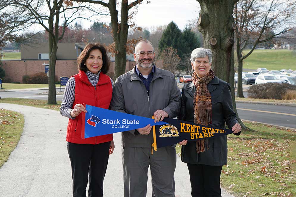 Three people holding college and university pennants on trail